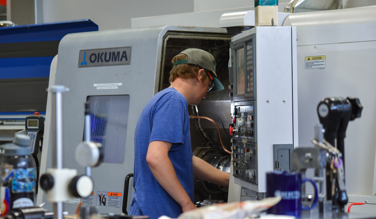 CNC Lathe Machinist II loads parts into Okuma lathe